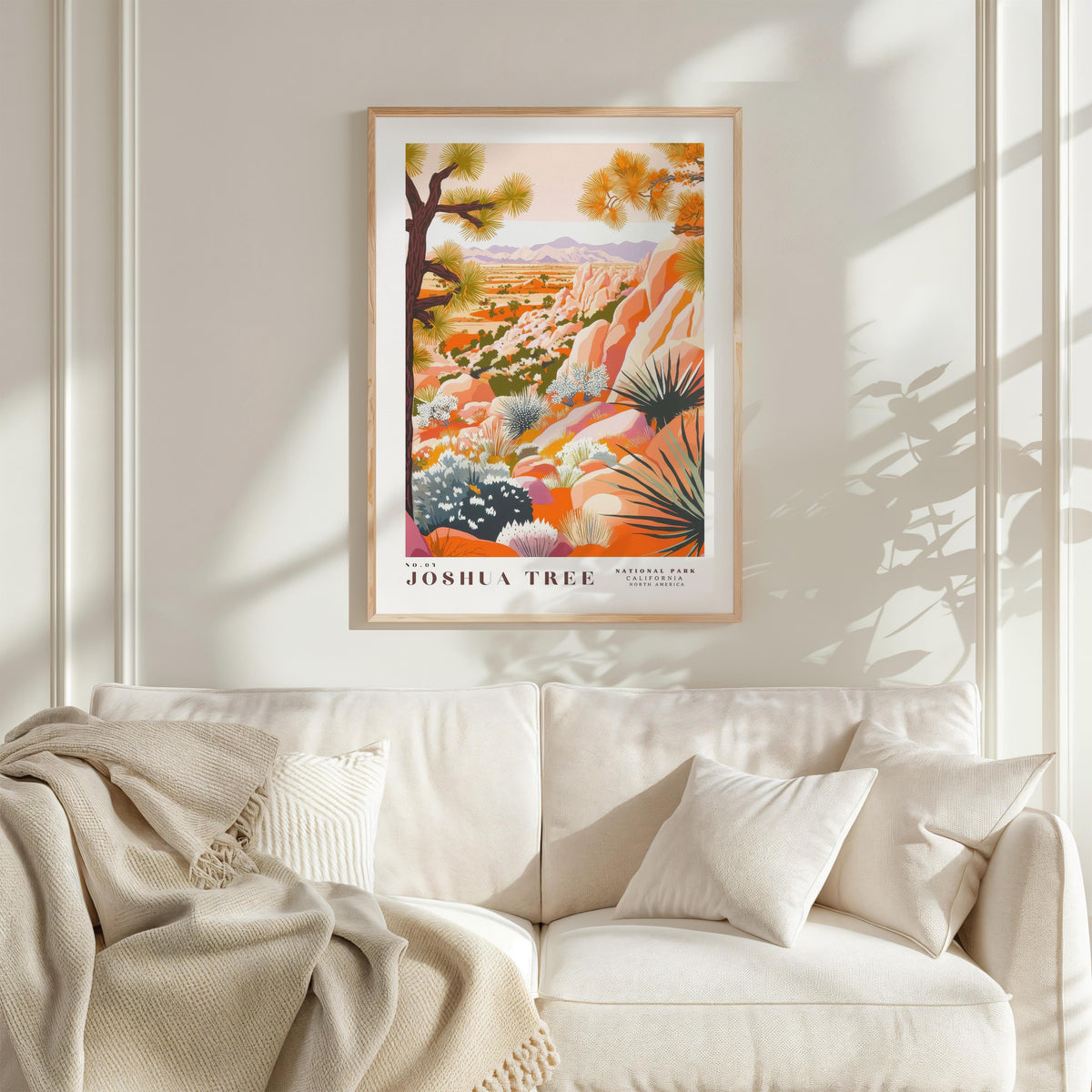 a framed poster of a desert landscape with a tree, hanging on a wall above a white couch with a blanket draped over it.