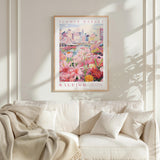 a framed poster of a cityscape with a flower market in the background, hanging on a wall above a white couch with a blanket draped over it.