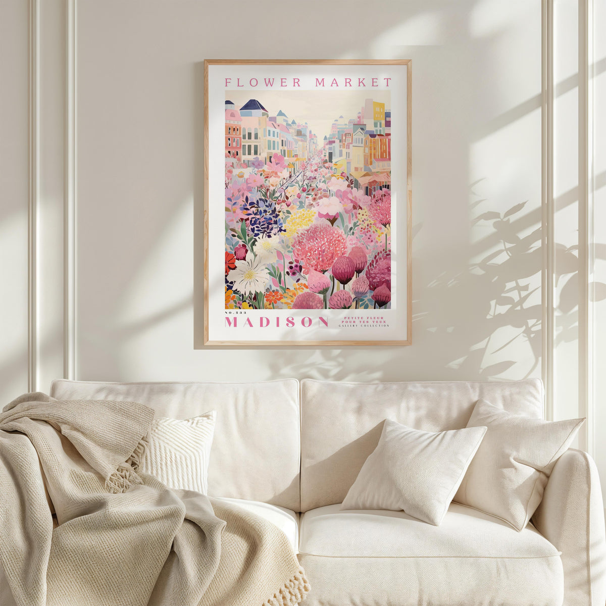 a framed poster of a colorful floral scene hanging on a wall above a white couch with a blanket draped over it.