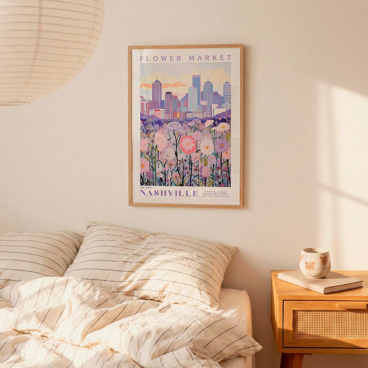 a bedroom setting with a framed poster of a cityscape and flowers hanging on the wall above a bed with striped pillows.
