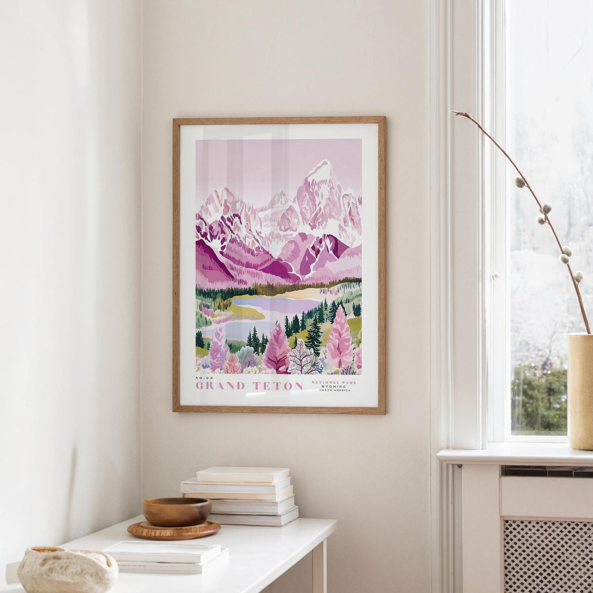 a framed poster of a scenic mountain landscape, hanging on a wall in a room with a white table and a window.