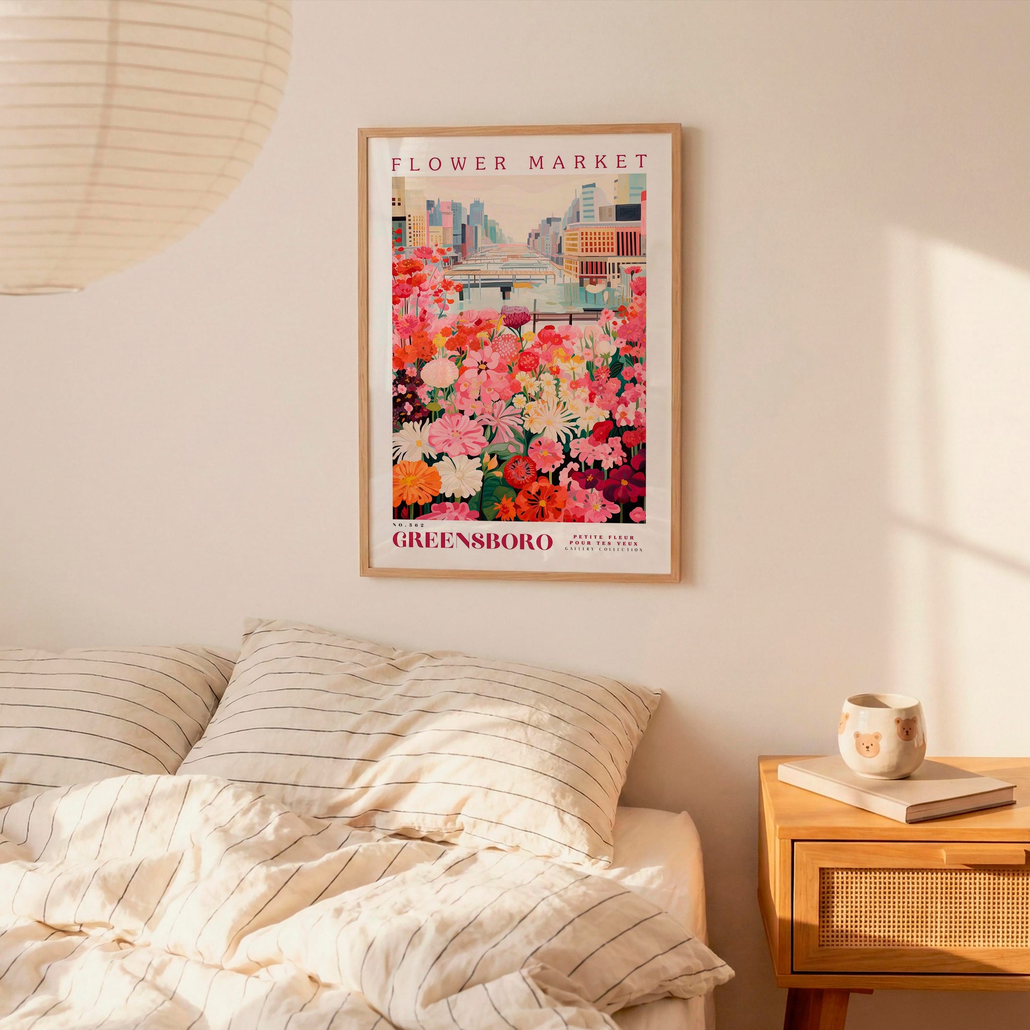 a bedroom scene with a framed poster of a flower market hanging on the wall above a bed with striped pillows.