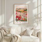 a framed poster of a field of flowers hanging on a wall above a white couch with pillows.