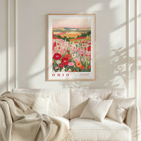 a framed poster of a field of flowers hanging on a wall above a white couch with pillows.