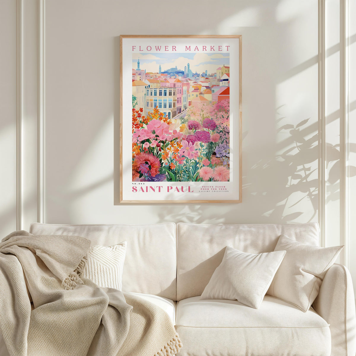 a framed poster of a colorful floral scene hanging on a wall above a white couch with a blanket draped over it.