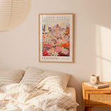 a bedroom setting with a framed poster of a flower market hanging on the wall above a bed with striped pillows.