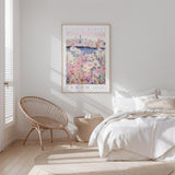 a bedroom with a bed, a woven chair, and a framed poster of a cityscape with flowers hanging on the wall.