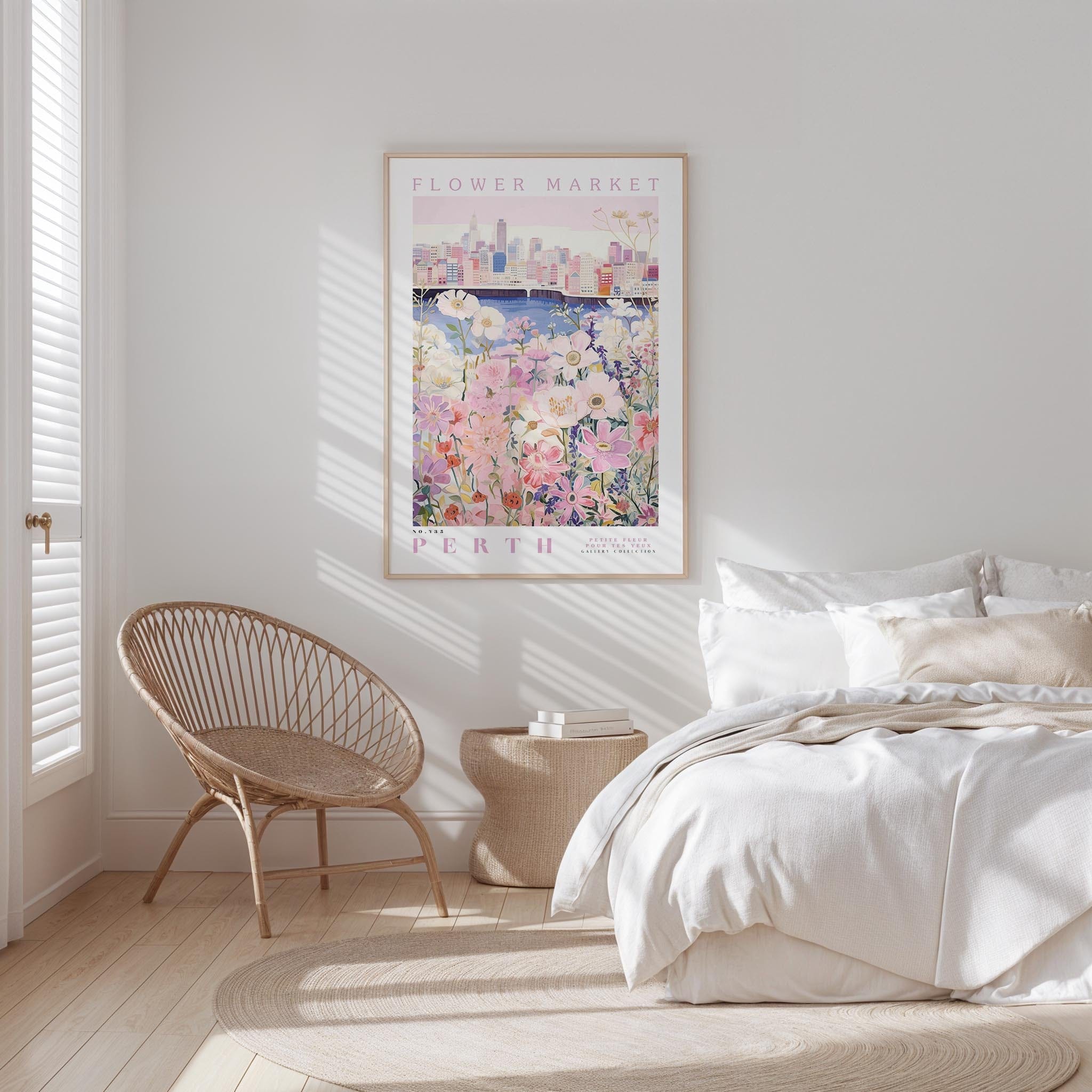 a bedroom with a bed, a woven chair, and a framed poster of a cityscape with flowers hanging on the wall.