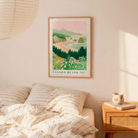 a bedroom scene with a framed poster of a coastal landscape hanging on the wall above a bed with striped pillows.