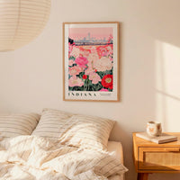 a bedroom setting with a framed poster of a field of flowers hanging on the wall above a bed with striped pillows.