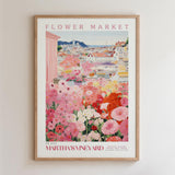 The image is a framed poster depicting a vibrant flower market scene with a variety of colorful flowers and buildings in the background.