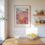 a kitchen scene with a framed poster of a colorful flower market in Newark hanging on the wall above a wooden counter. On the counter, there is a bowl of lemons and a plant.