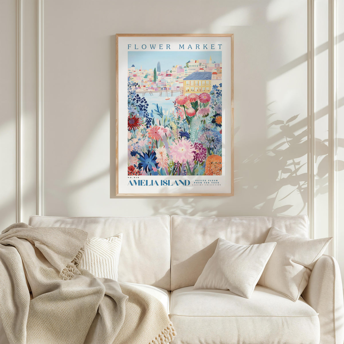 a poster of the "Flower Market" on a wall, with a white sofa and a blanket in the foreground.