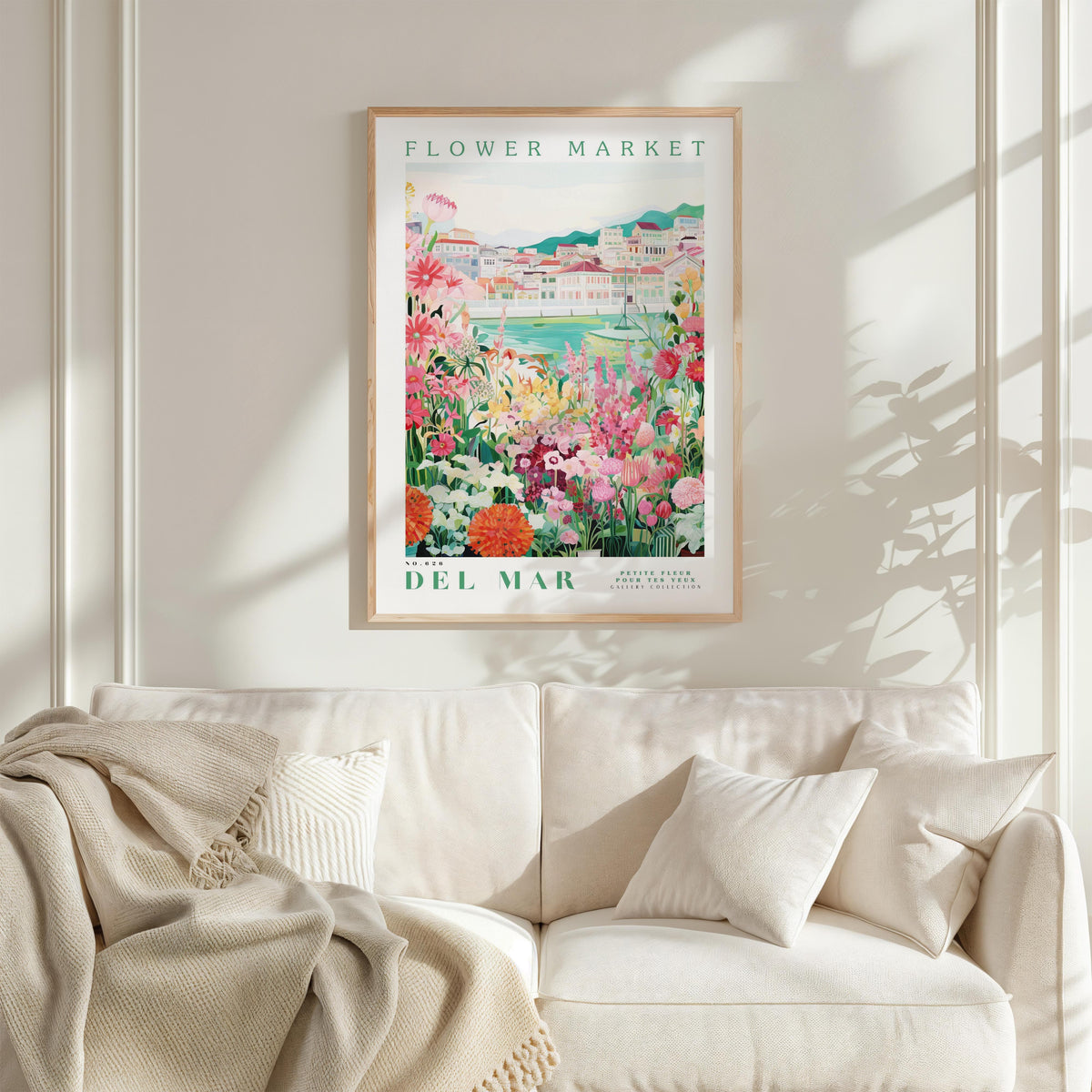 a framed poster of a colorful garden scene hanging on a wall above a white couch with a blanket draped over it.