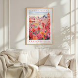 a framed poster of a vibrant floral scene hanging on a wall above a white couch with a blanket draped over it.