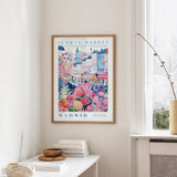 a framed poster of a colorful street scene in Madrid, Spain, hanging on a wall.