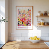 a kitchen counter with a bowl of lemons, a framed poster of a flower market, and shelves with jars and containers.