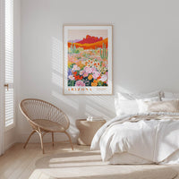 a bedroom with a bed, a woven chair, and a framed poster of a desert landscape with cacti and flowers.