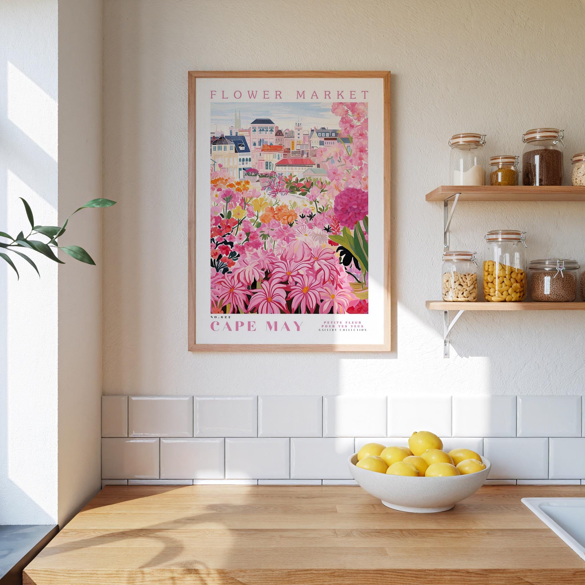 a kitchen scene with a framed poster of a colorful flower market in Cape May, New Jersey, hanging on the wall above a wooden counter. On the counter, there is a bowl of lemons and a plant.