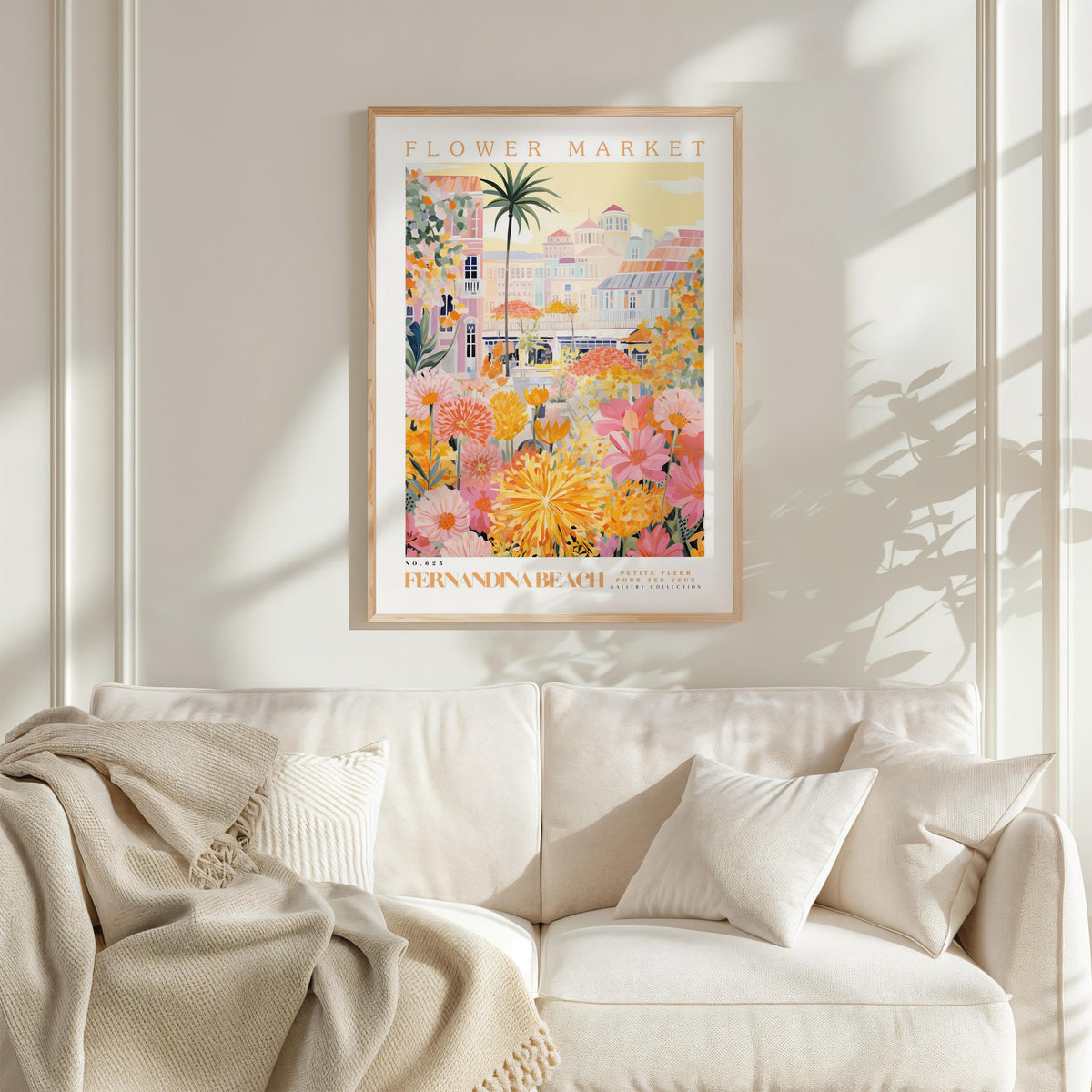 a framed poster of a colorful, tropical garden scene hanging on a wall above a white couch with a blanket draped over it.