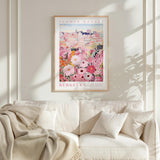 a framed poster of a colorful floral scene hanging on a wall above a white couch with a blanket draped over it.
