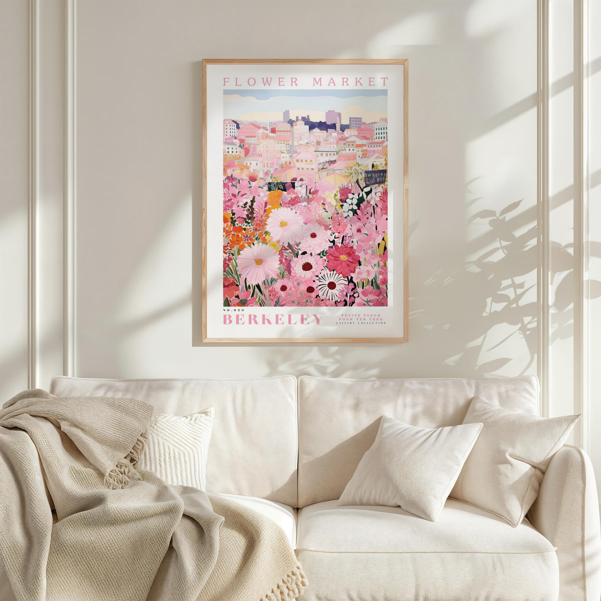 a framed poster of a colorful floral scene hanging on a wall above a white couch with a blanket draped over it.
