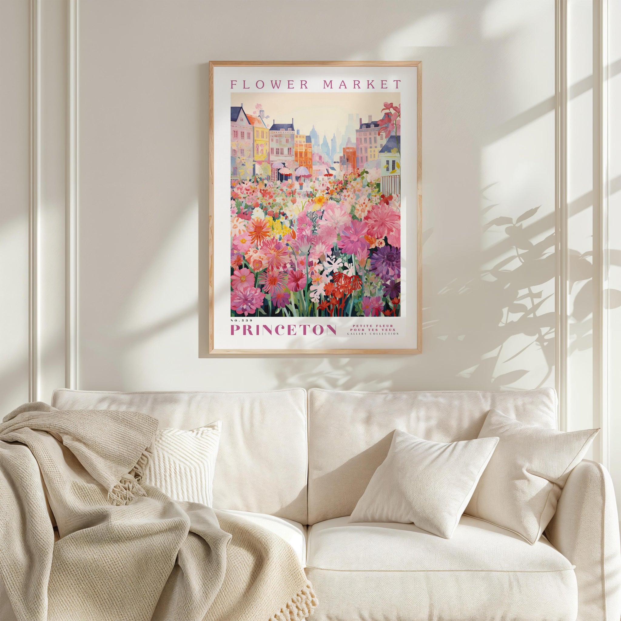 a framed poster of a colorful floral scene hanging on a wall above a white couch with a blanket draped over it.