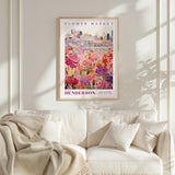 a framed poster of a colorful floral scene hanging on a wall above a white couch.