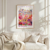 a framed poster of a colorful floral scene hanging on a wall above a white couch.