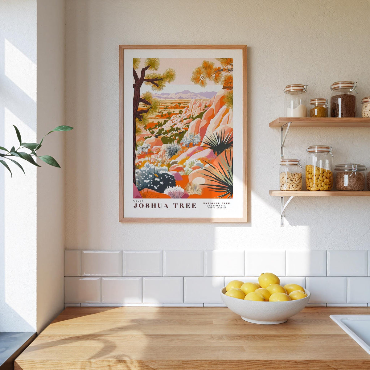 a kitchen counter with a bowl of lemons, a framed poster of Joshua Tree, and various jars and containers on a shelf.