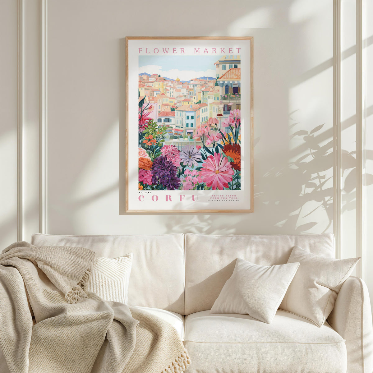 a framed poster of a colorful floral scene hanging on a wall above a white couch with a blanket draped over it.