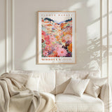 a poster of a flower market in Missoula, Montana, hanging on a wall above a white couch with a blanket draped over it.