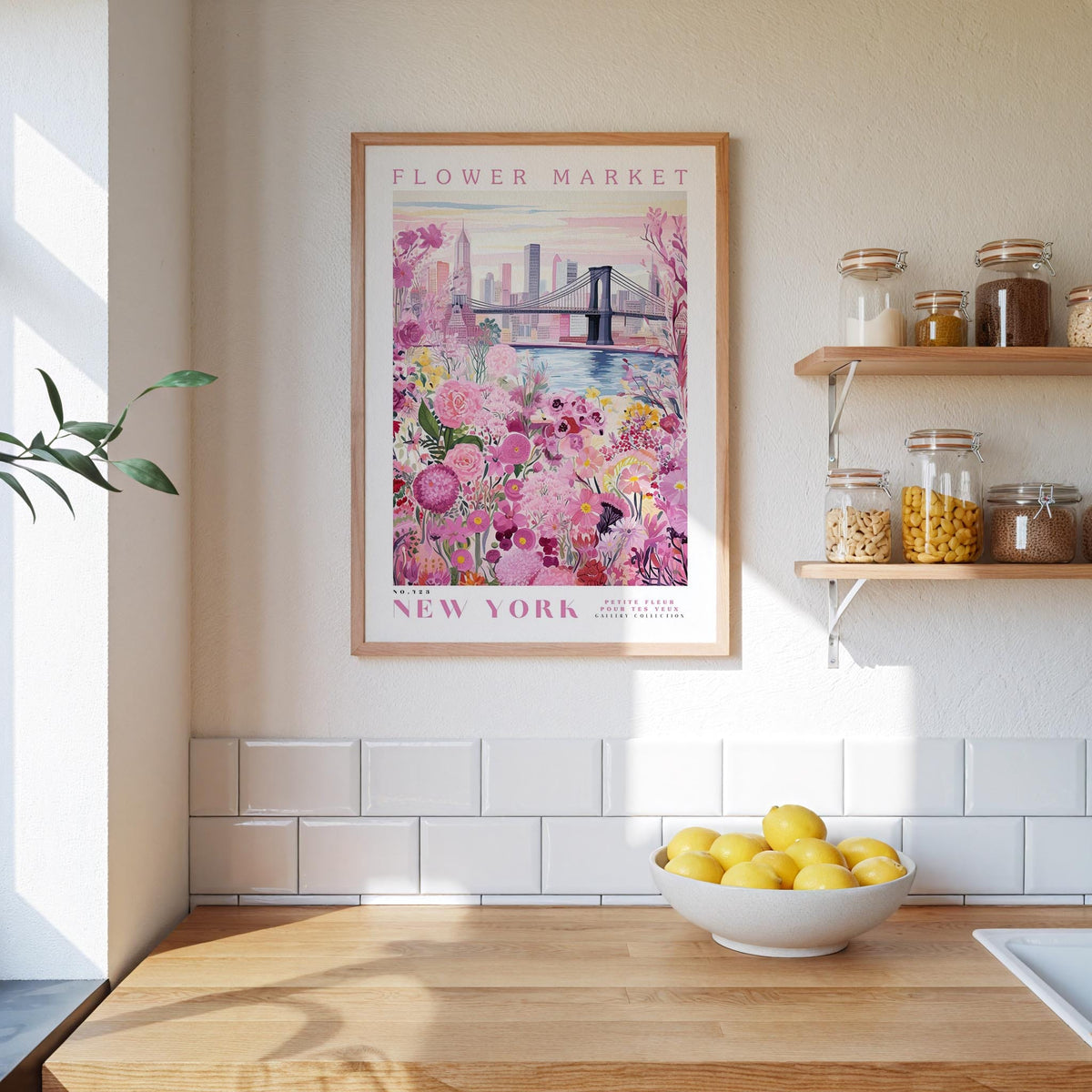 a kitchen counter with a bowl of lemons, a framed poster of a flower market in New York, and a shelf with jars and other kitchen items.