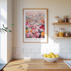 a framed poster of a colorful floral scene hanging on a wall above a wooden countertop with a bowl of lemons.