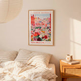 a bedroom setting with a framed poster of a colorful flower market in New Orleans hanging on the wall above a bed with striped pillows.