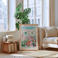 a living room with a large window, a white sofa, a wooden side table with books, and a framed poster of a flower market in Greece.