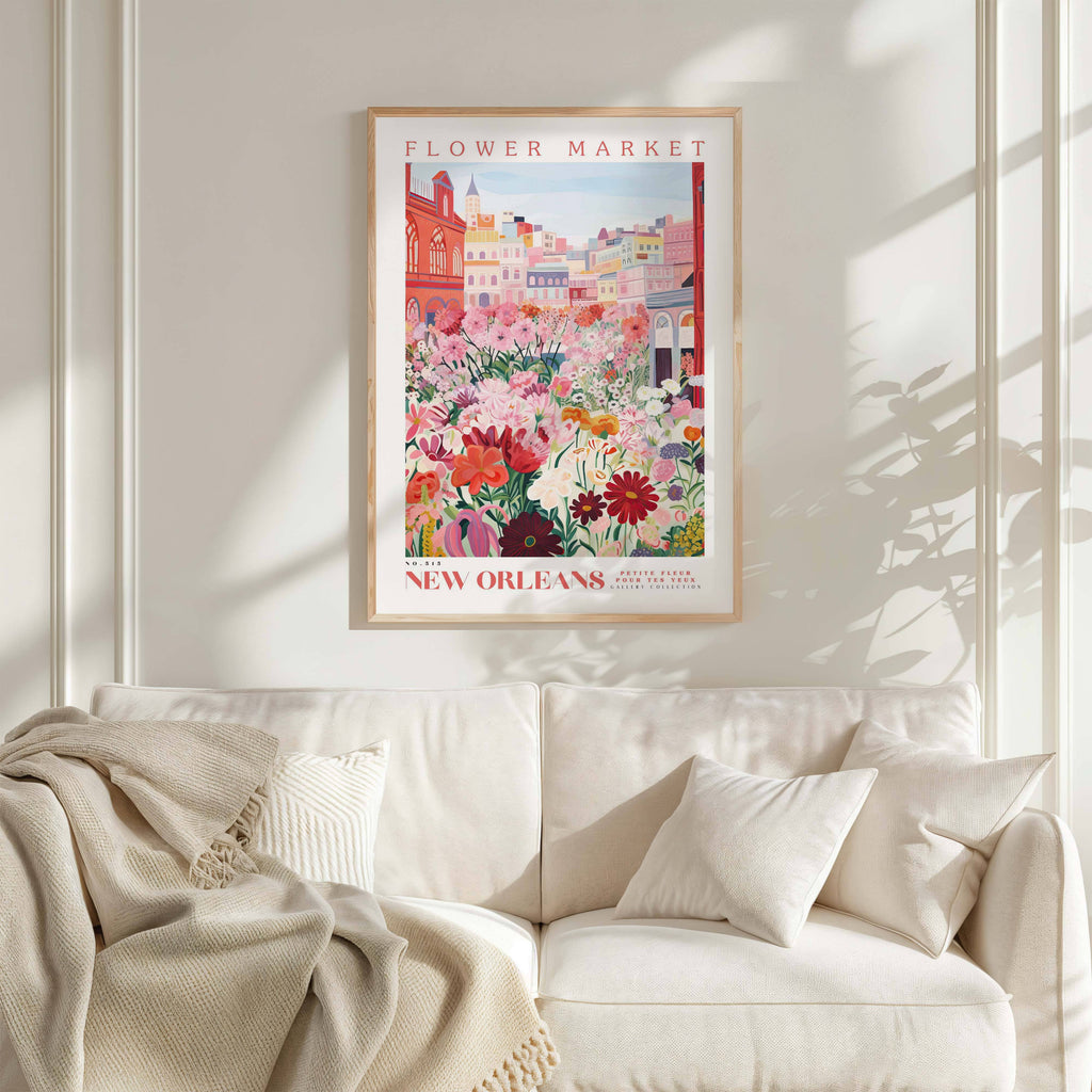 a framed poster of a colorful floral scene hanging on a wall above a white couch with a blanket draped over it.