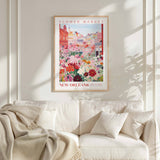 a framed poster of a colorful floral scene hanging on a wall above a white couch with a blanket draped over it.