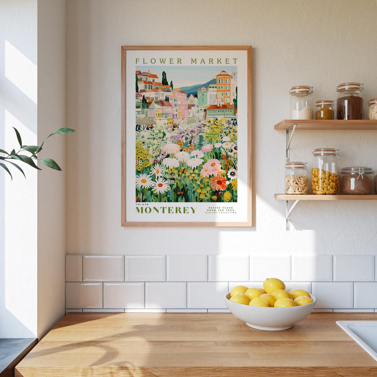 a framed poster of a flower market in Monterey, California, hanging on a wall above a kitchen counter with a bowl of lemons and jars of food on the counter.