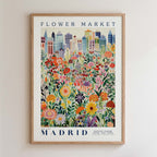 The image is a framed poster depicting a vibrant and colorful cityscape with a variety of flowers and plants in the foreground.