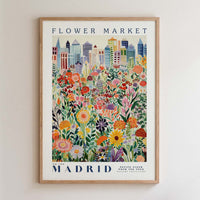 The image is a framed poster depicting a vibrant and colorful cityscape with a variety of flowers and plants in the foreground.