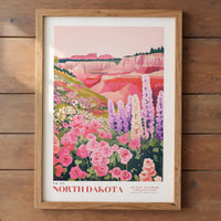 The image is a framed poster depicting a scenic landscape of the North Dakota state flower collection, featuring a vibrant field of pink and white flowers against a backdrop of mountains and cliffs.