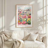 a cozy living room with a white sofa and a framed poster of a colorful garden scene hanging on the wall above it.