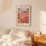 a bedroom setting with a framed poster of a colorful flower market in New York hanging on the wall above a bed with striped pillows.