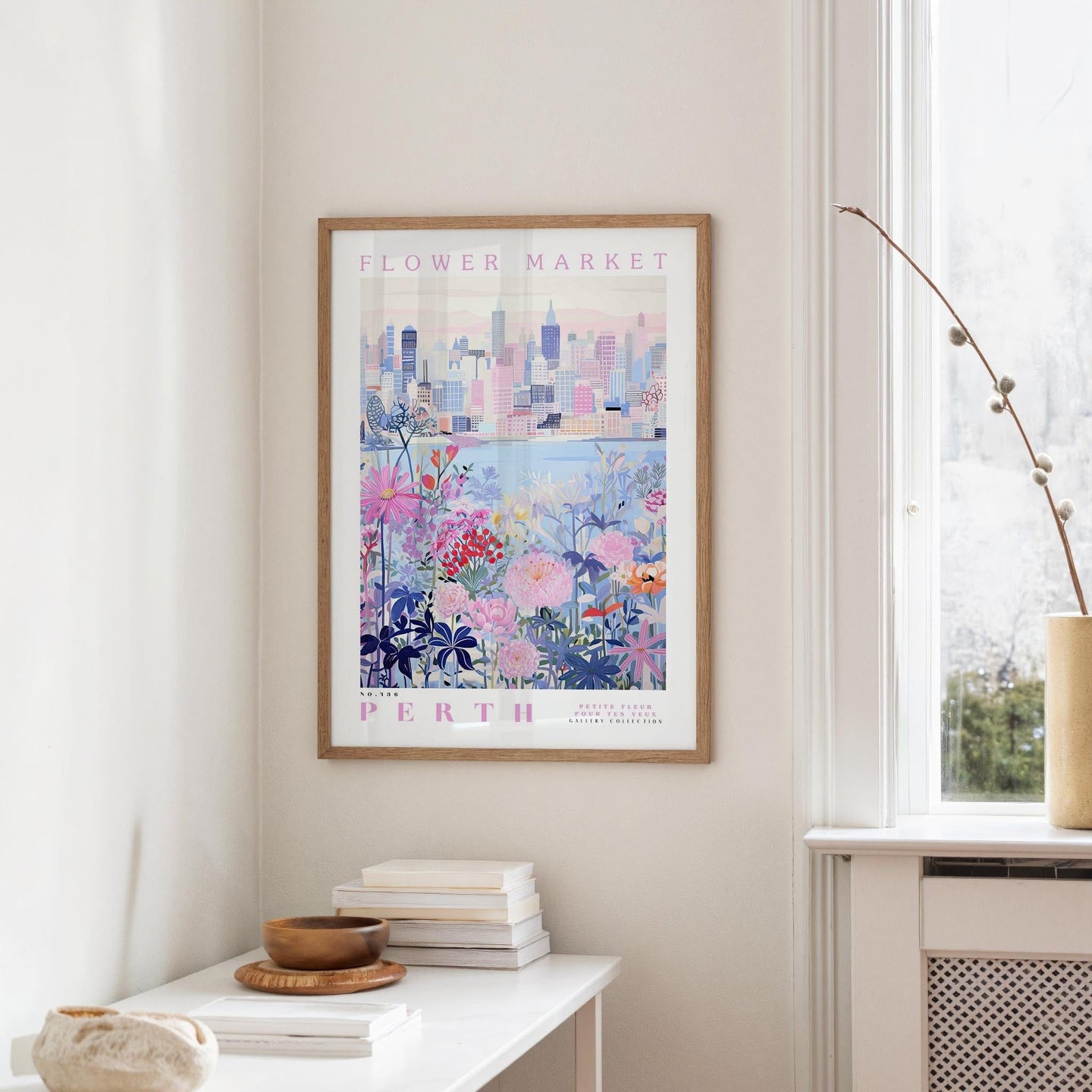 a framed poster of a cityscape with a floral design, hanging on a wall in a room with a white table and a window.