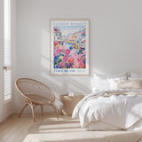 a bedroom with a large poster of a flower market hanging on the wall, a wicker chair, and a bed with white bedding.