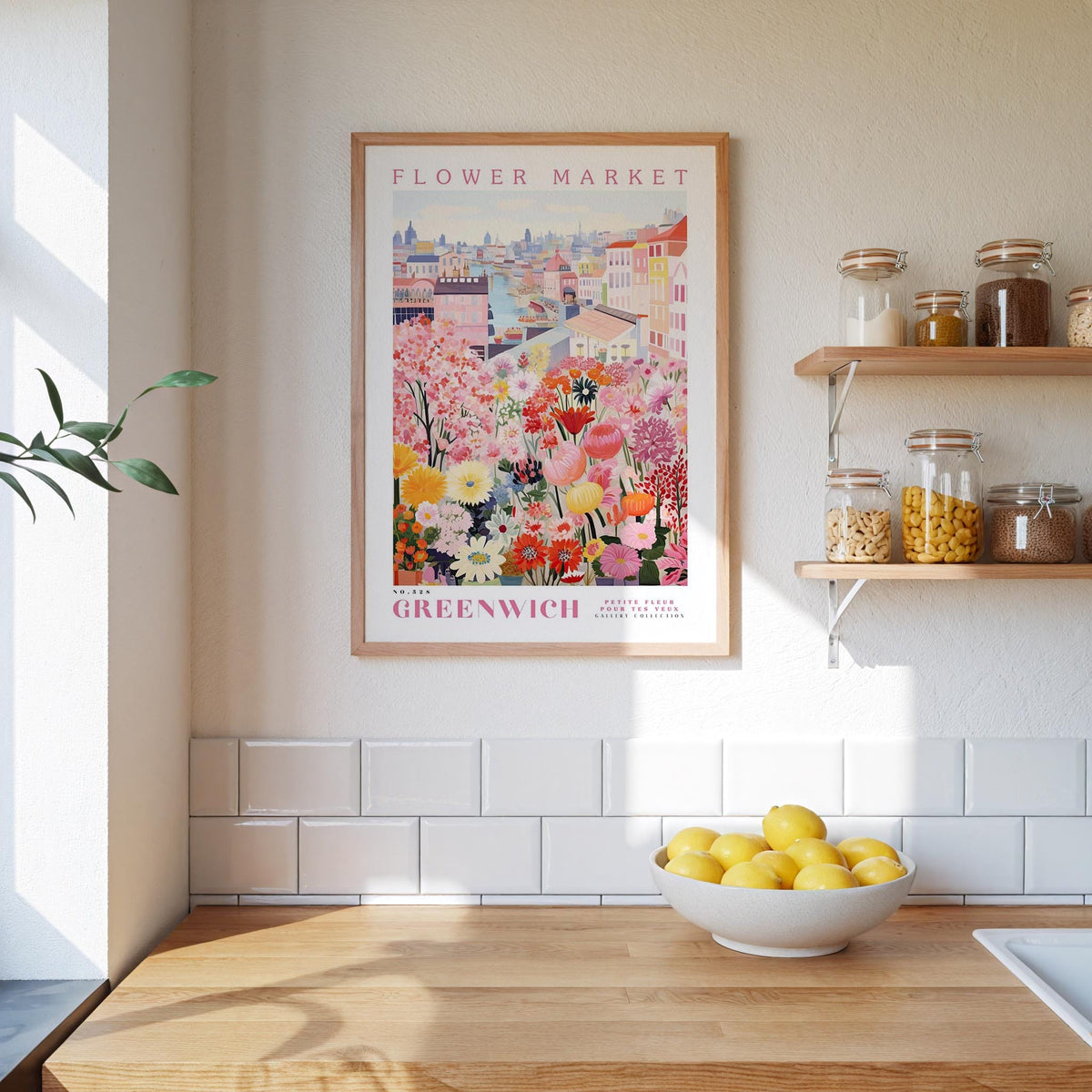 a kitchen scene with a framed poster of a colorful flower market in Greenwich, London, hanging on the wall above a wooden counter. The poster displays a variety of flowers and plants, creating a vibrant and lively atmosphere. On the counter, there is a bowl of lemons, adding a touch of freshness to the scene. The kitchen also includes shelves with jars and bottles, as well as a sink, contributing to the overall homey and welcoming ambiance.