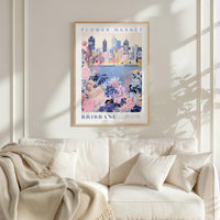a framed poster of a cityscape with a floral design, hanging on a wall above a white couch with pillows.
