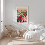 a bedroom with a large framed poster of a garden hanging on the wall, a woven chair, and a bed with white bedding.