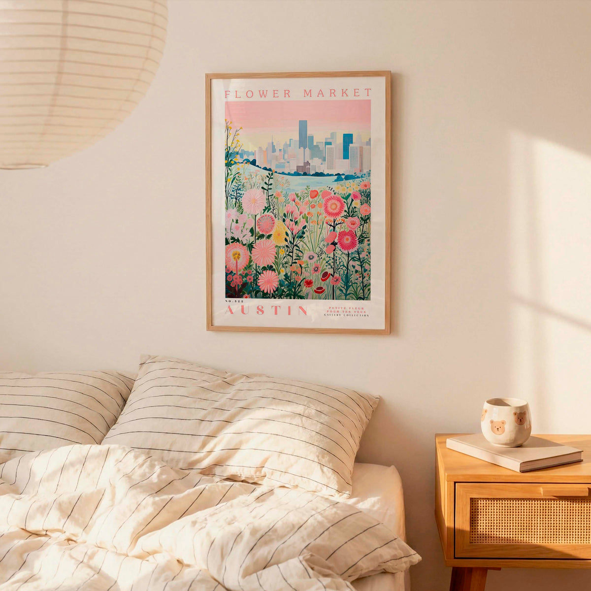 a bedroom scene with a framed poster of a flower market in Austin hanging on the wall above a bed with striped pillows.